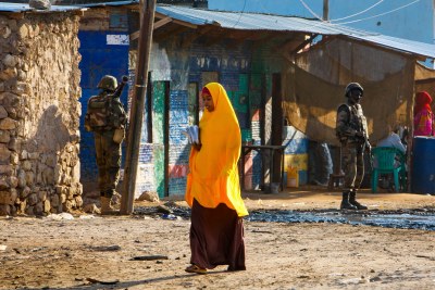 A Somali girl crosses a street on her way to school while soldiers of AMISOMs Djiboutian contingent stand guard (file photo).