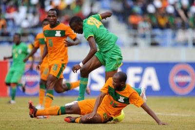 Christopher Munthali of Zambia goes in low to tackle Tendai Ndoro of Zimbabwe.