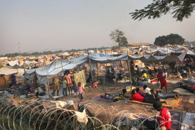 Des enfants et des adultes déplacés s’abritent à l’extérieur d’une clôture de barbelés, dans un camp mis en place derrière l’aéroport international Mpoko de Bangui, en République centrafricaine (RCA).